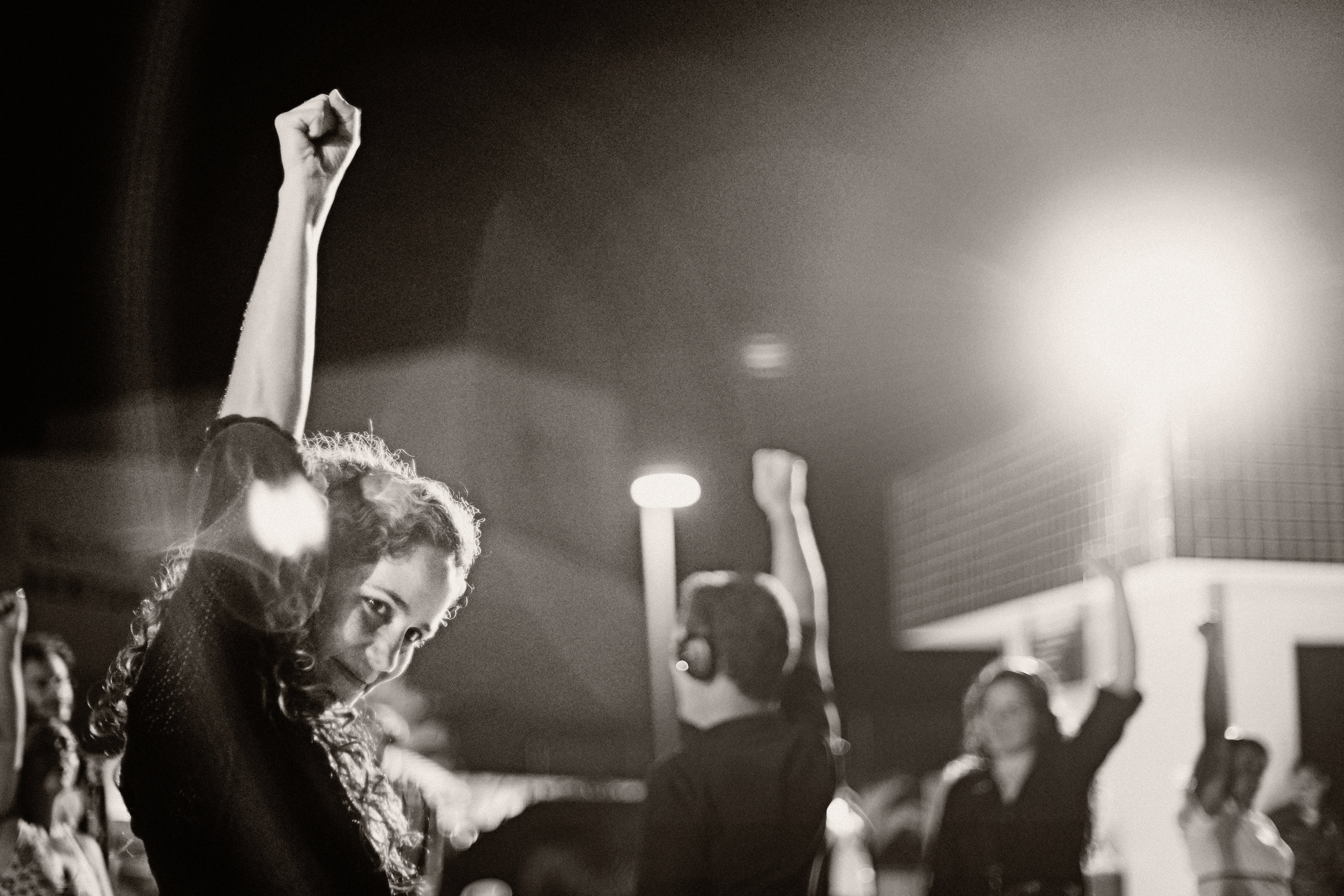 image description: in foreground: a woman, wearing headphones, with her fist in the air. In background: more people—all with headphones on—with their fists raised.