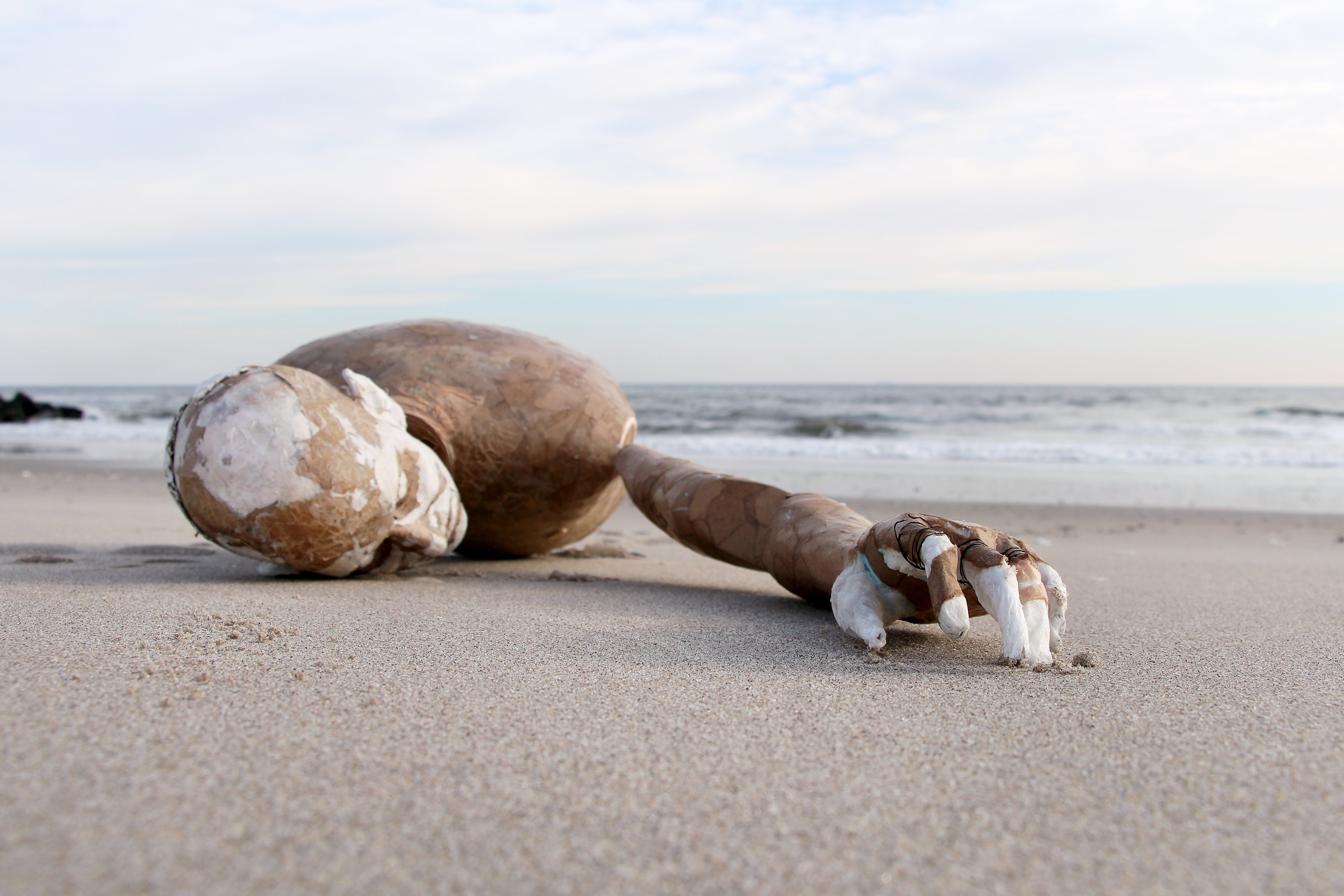 Image description: a mannequin washed on the shore of the beach, its arm stretched out towards the camera.