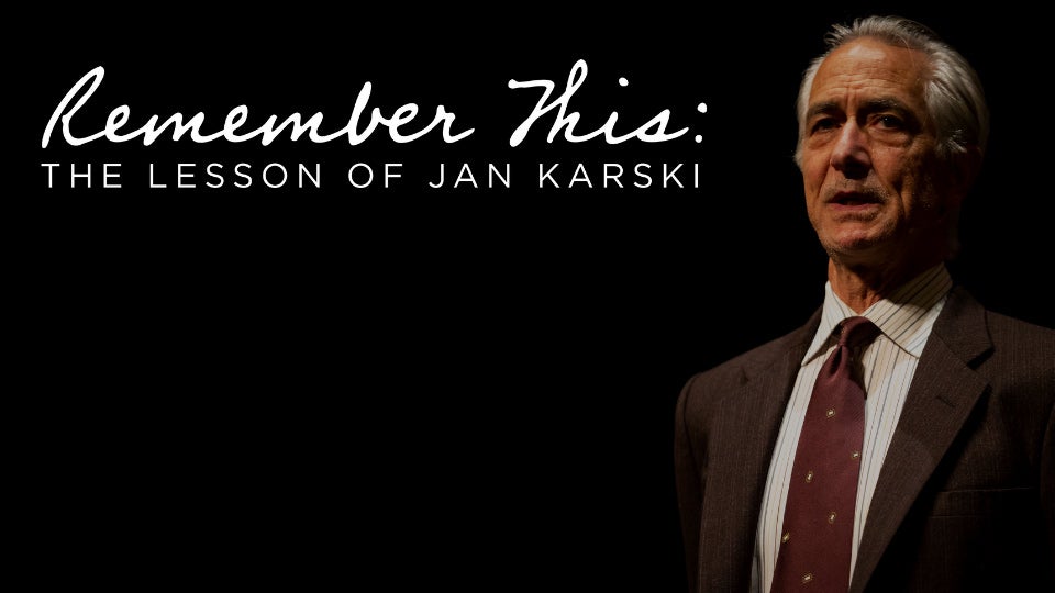 Older man in a suit stands on a dark stage. White text reads "Remember This: The Lesson of Jan Karski"