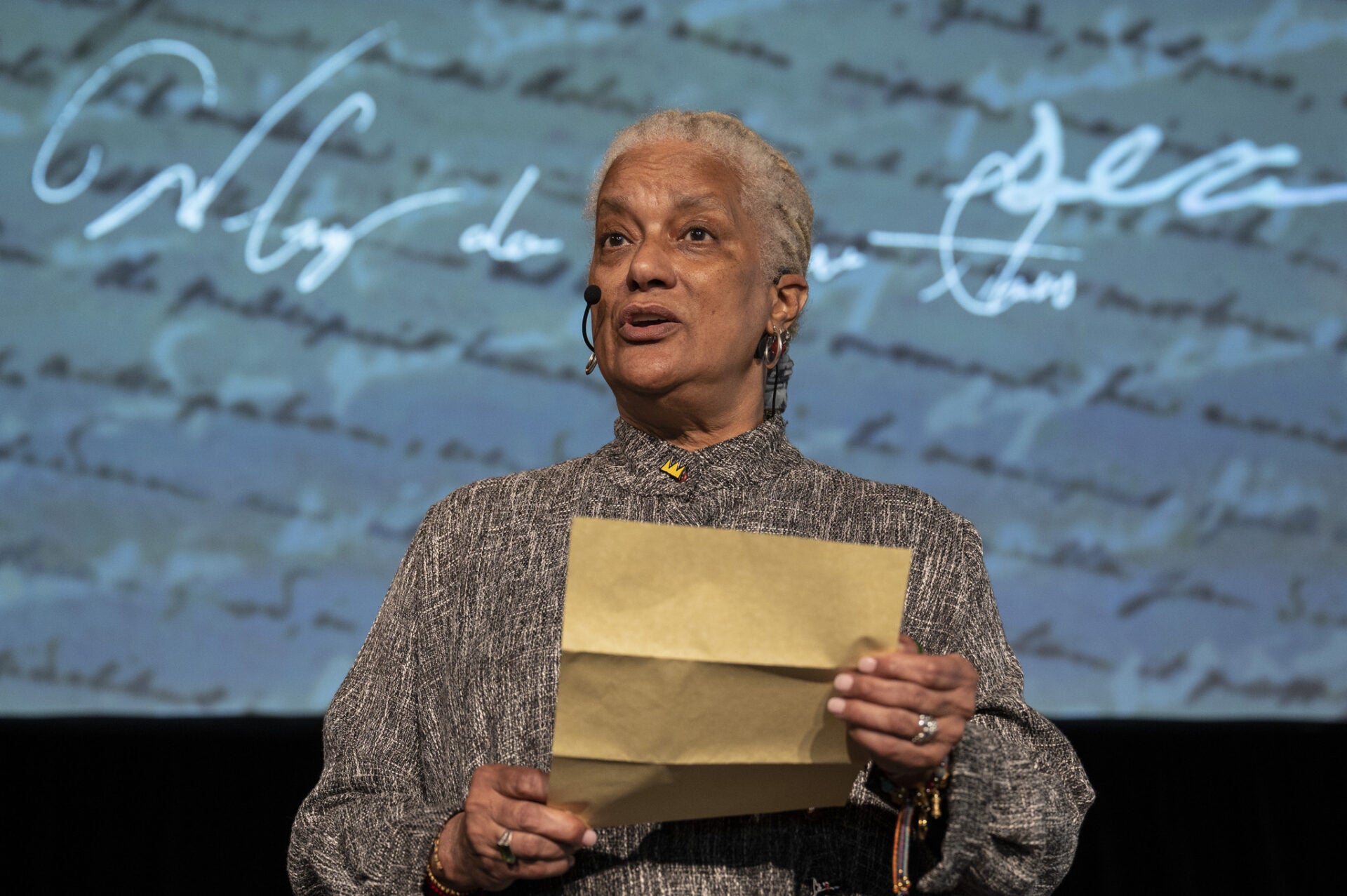 Older woman reads from a piece of paper and wears a handsfree microphone
