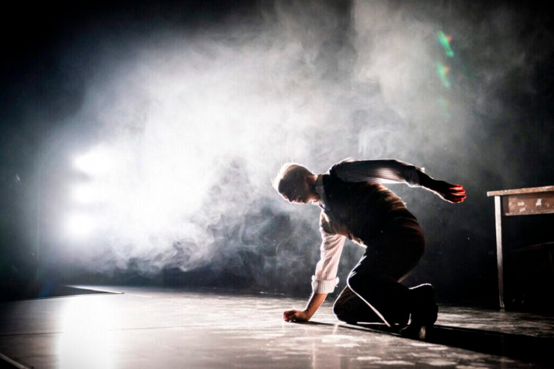 Backlit on a smoky stage, an older man falls to his knees during a performance