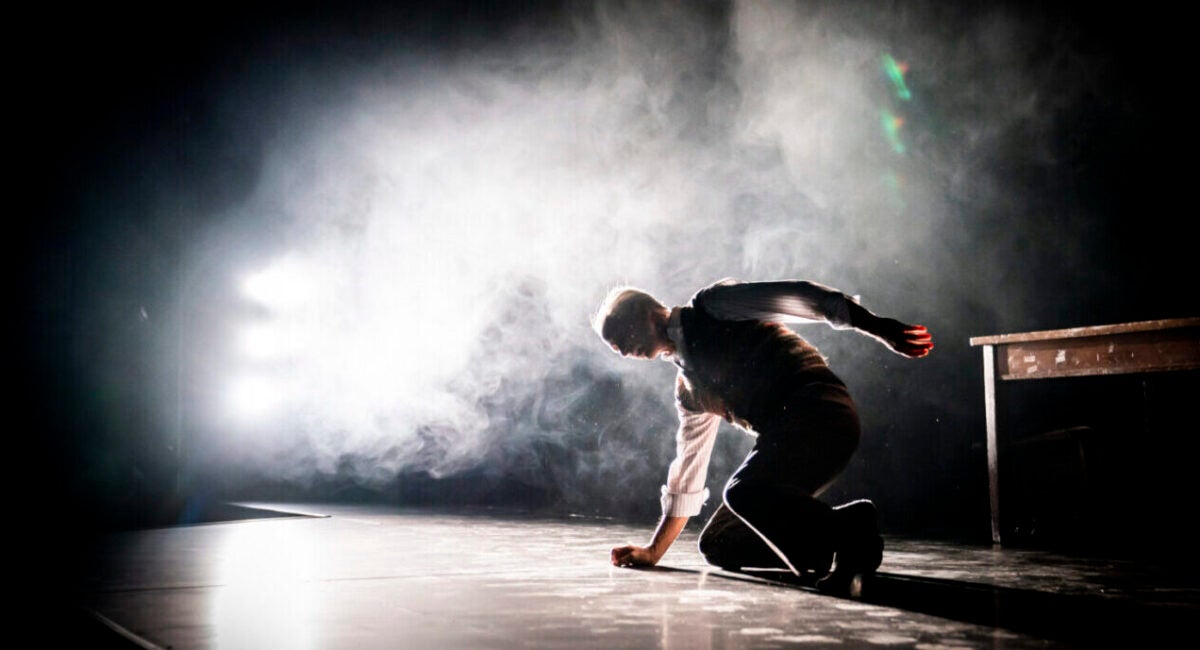 Backlit on a smoky stage, an older man falls to his knees during a performance